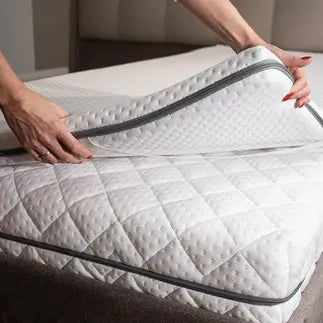 Frau legt Elastica Topper auf eine Matratze mit sichtbarem Reißverschluss